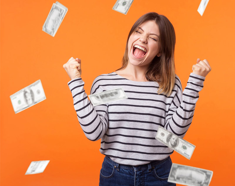 Woman with brown hair and yellow sweater holding 16 100 dollar bills celebrating on a tan background