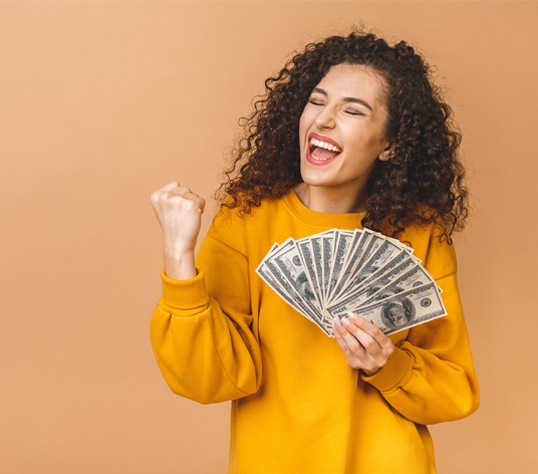 Woman with brown hair and yellow sweater holding 16 100 dollar bills celebrating on a tan background