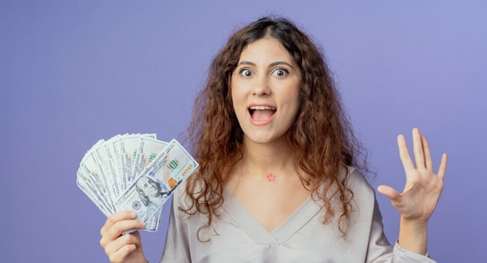 Woman excitedly holding cash, representing quick access to funds from payday loans, against a purple background.